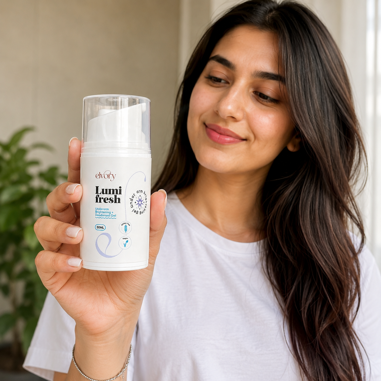 A woman with long dark hair holds up a white pump bottle of Elvory's Lumi Fresh underarm gel.